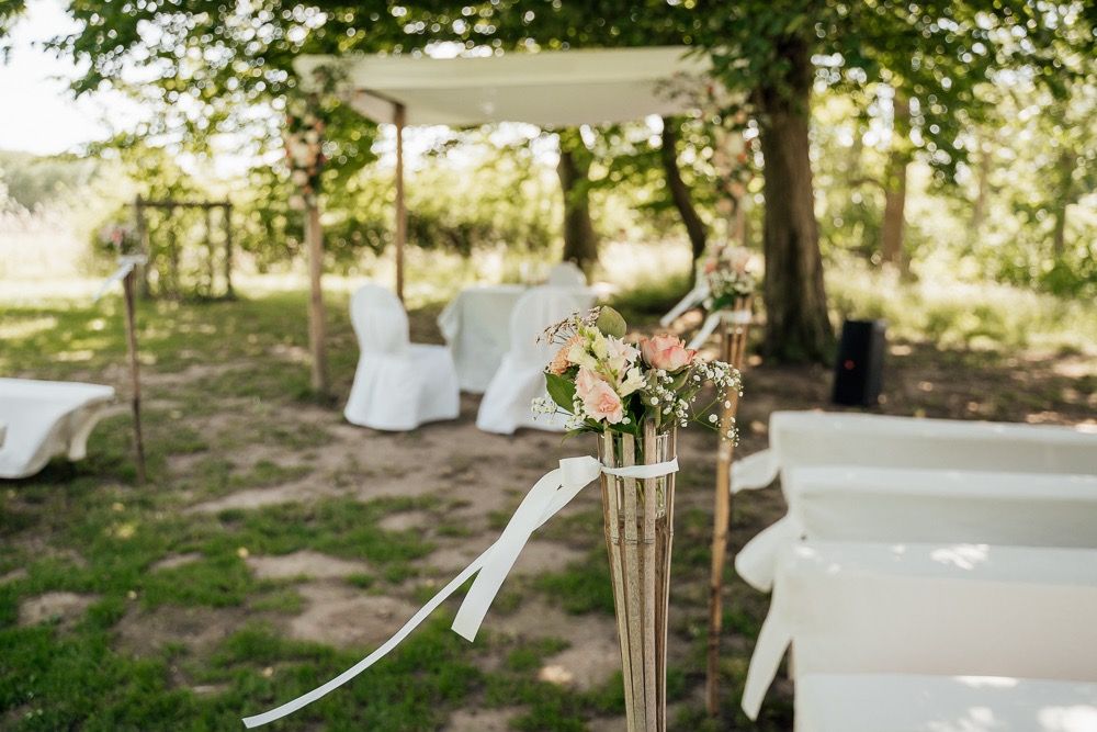 White wedding ceremony setup in an outdoor garden with tall floral arrangements and flowing drapery.