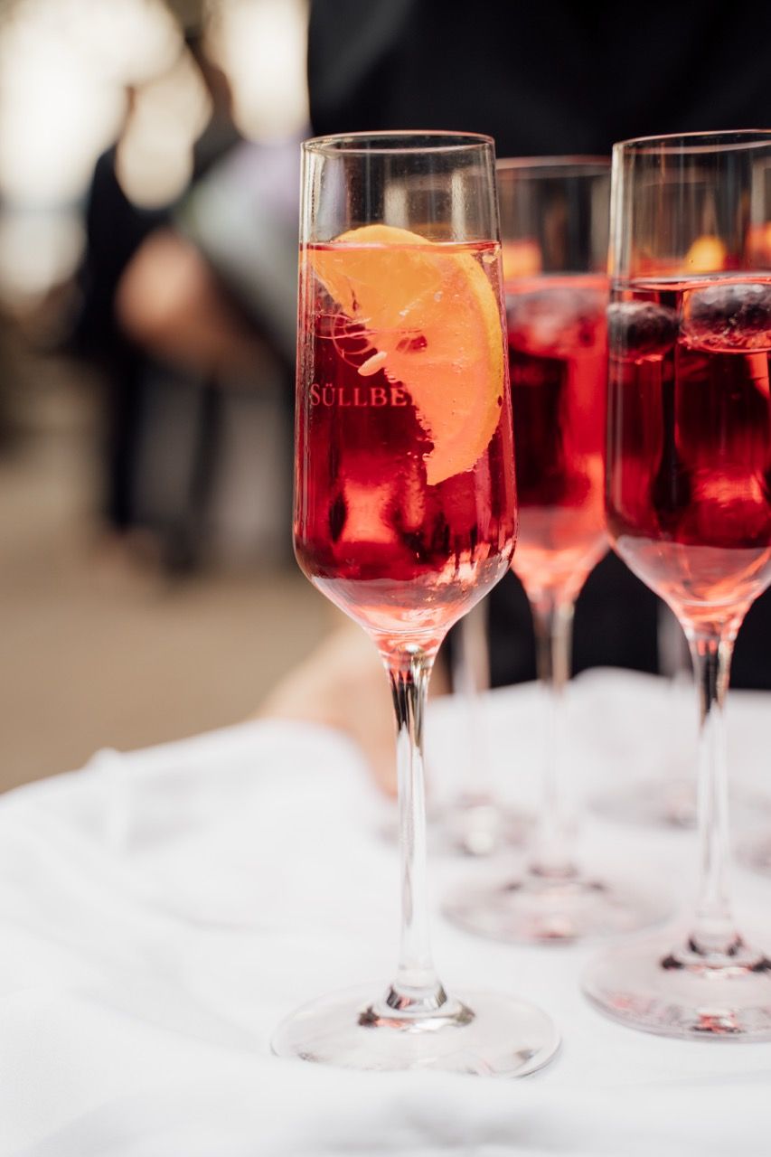 Elegant champagne flutes filled with red cocktails garnished with orange slices on a white tray at an event.