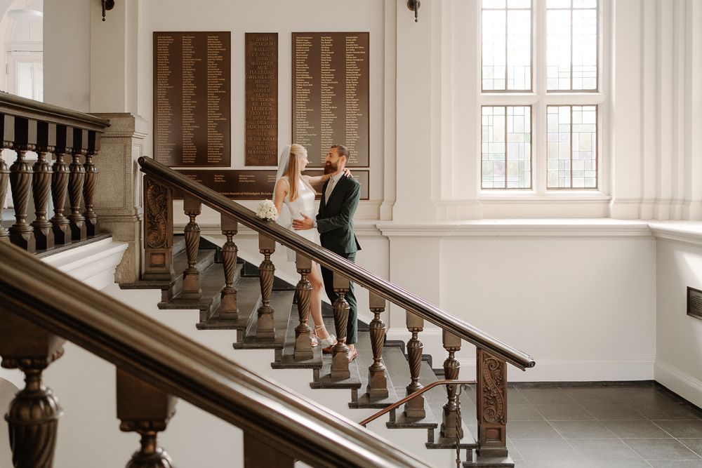 A person in formal attire walks up an elegant white staircase in what appears to be a historic building.