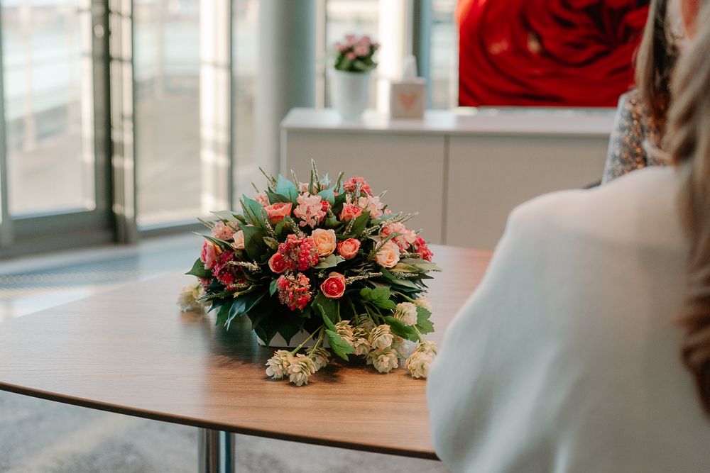 A beautiful floral arrangement with pink roses and greenery sits on a wooden table near a window.