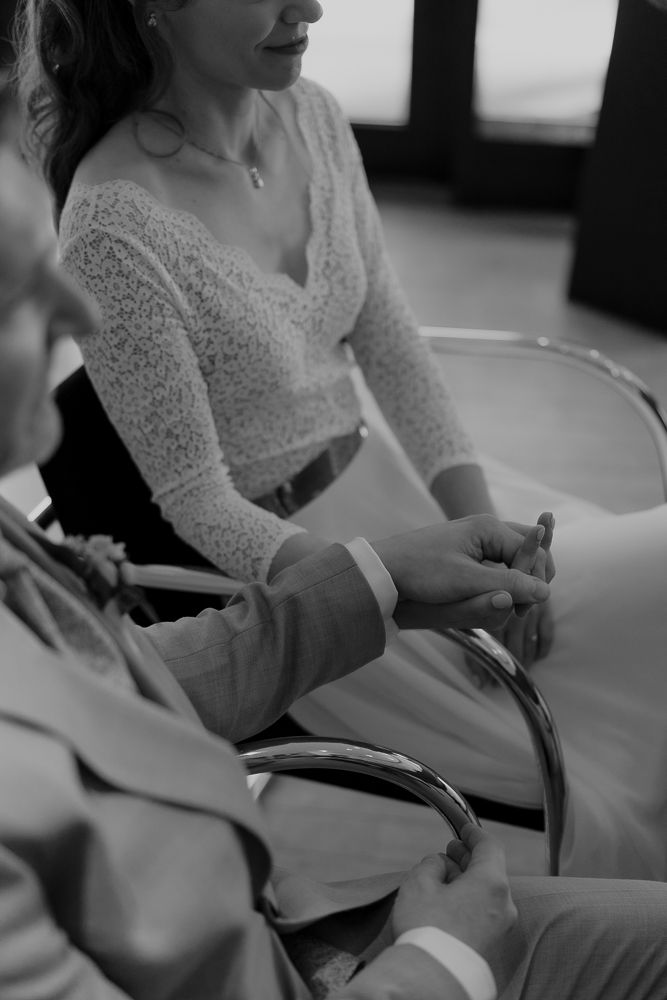 Black and white image shows a person wearing a lace dress adjusting something while sitting down.
