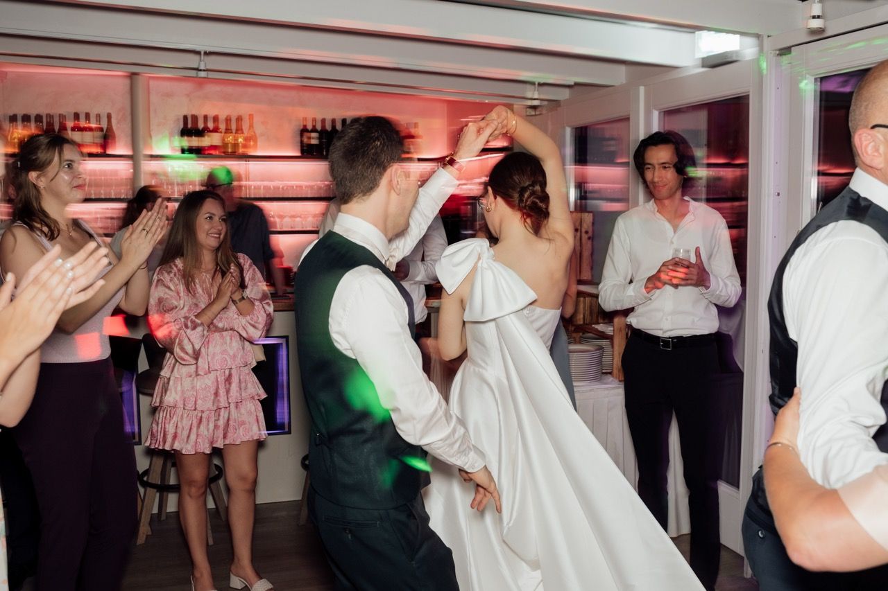 Bride and groom dancing together at wedding reception while guests clap and celebrate around them.