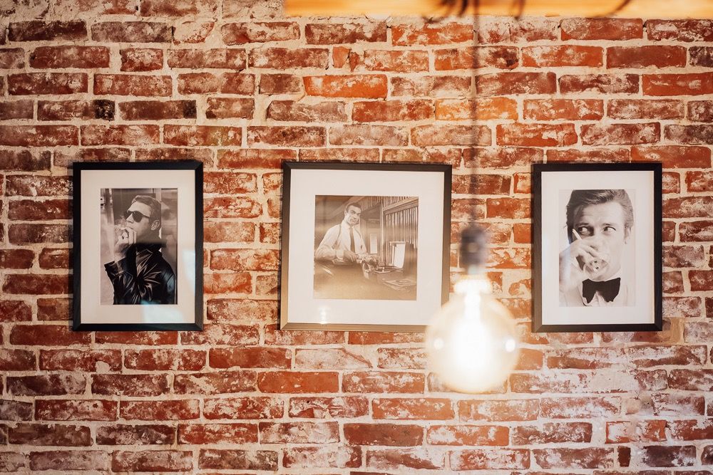 Vintage black and white photographs hang on an exposed brick wall illuminated by industrial pendant lighting.