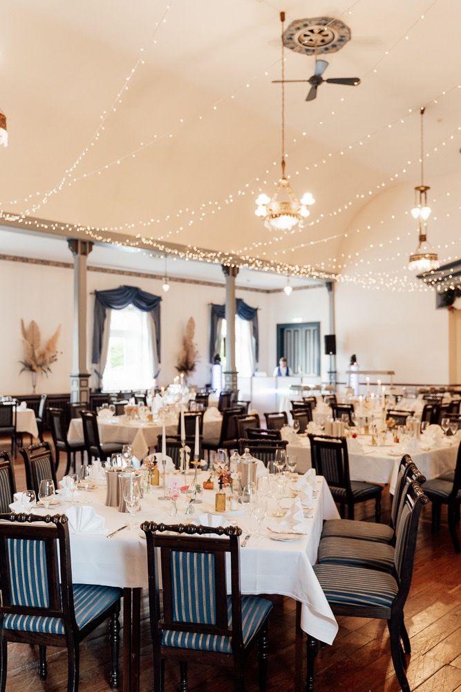 Elegant banquet hall with white tablecloths, blue-striped chairs, and twinkling string lights decorating the ceiling.