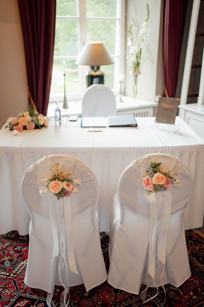 Elegant white chair covers with peach rose decorations and flowing ribbons at a wedding reception table setup.