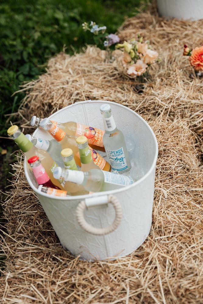 White heart-shaped container filled with chilled beverages on hay bales at an outdoor event.