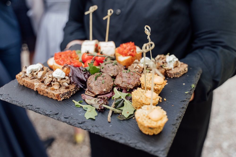 Elegant catering appetizers served on black slate platters with decorative wooden skewers at an upscale event.