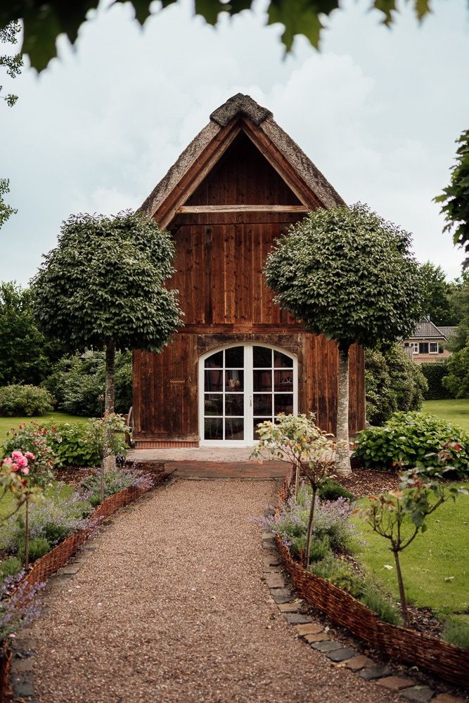 A charming rustic wooden chapel with white French doors and manicured garden path lined with flowering bushes.