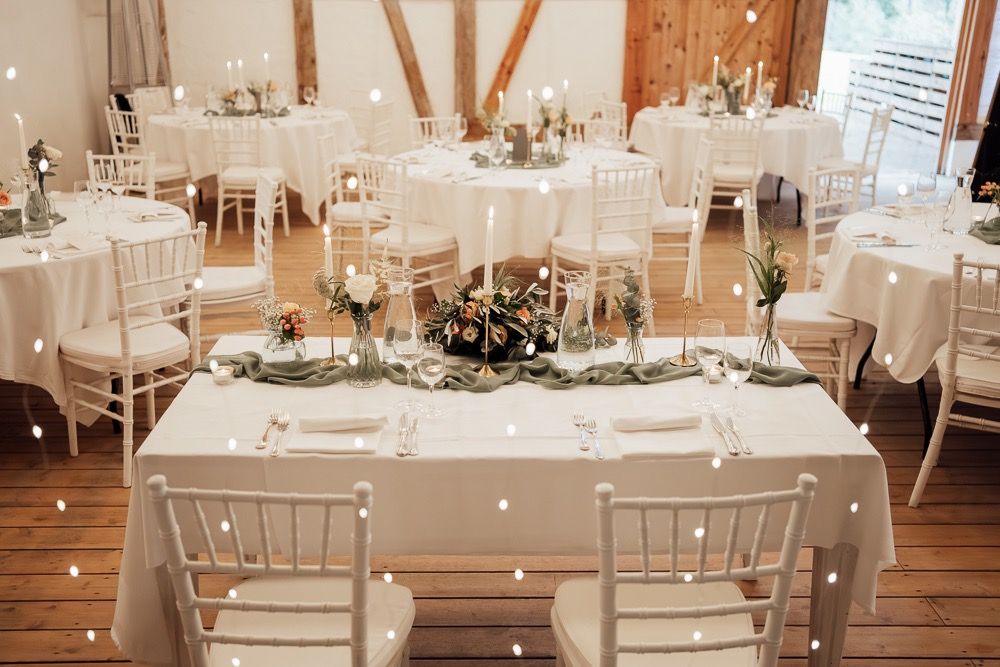 Elegant white wedding reception tables set with floral centerpieces in a rustic wooden barn venue.