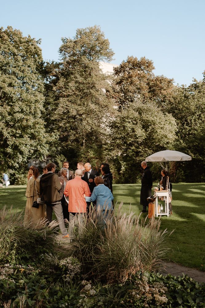 Small outdoor gathering in a garden setting with guests standing near ornamental grasses and trees at sunset.