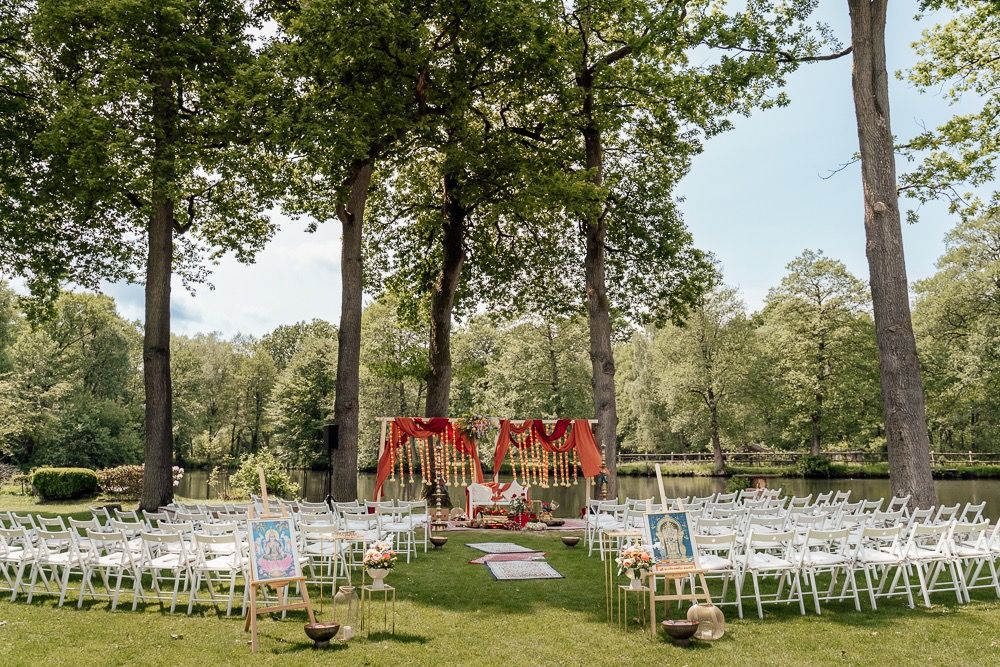 Panoramic view of an outdoor wedding ceremony setup with white chairs arranged in rows under tall trees.
