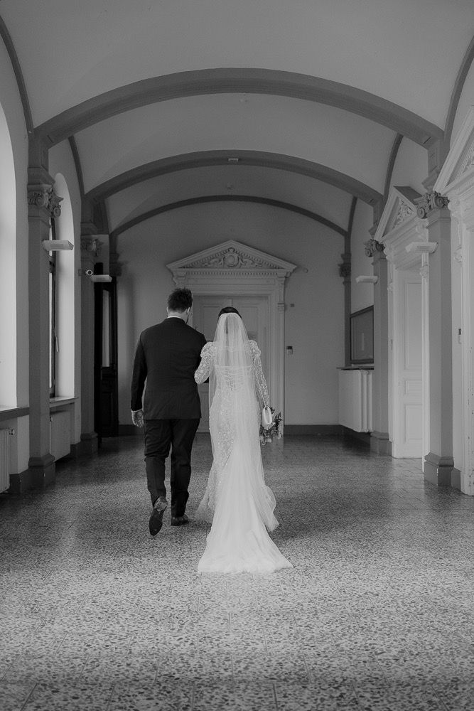 A black and white panoramic sequence showing a figure in white and dark silhouettes walking through an arched hallway.