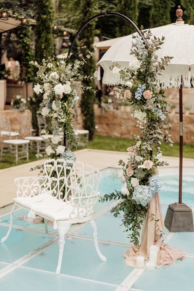 White poolside lounge chairs and umbrellas create an elegant outdoor setting with lush greenery and decorative arches.