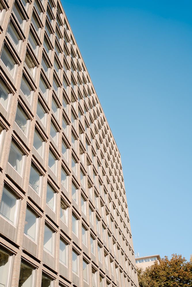 Modern office building facade with repeating geometric pattern of windows against bright blue sky.