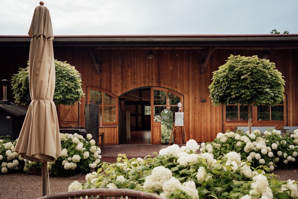 Rustic wooden wedding venue exterior decorated with white hydrangea flowers and beige umbrellas.