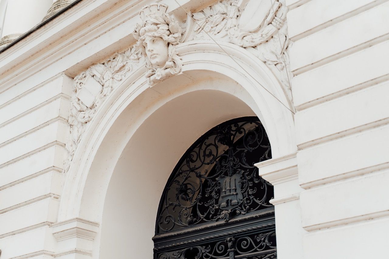 Ornate white architectural details frame an arched doorway with decorative ironwork in a classical building facade.