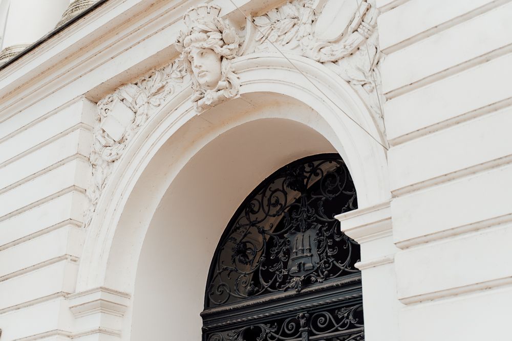 Ornate white architectural details with decorative molding and arched doorways along a classical building facade.