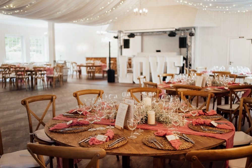 Elegant wedding reception venue with string lights, white draping, and rustic wooden tables set for a celebration.