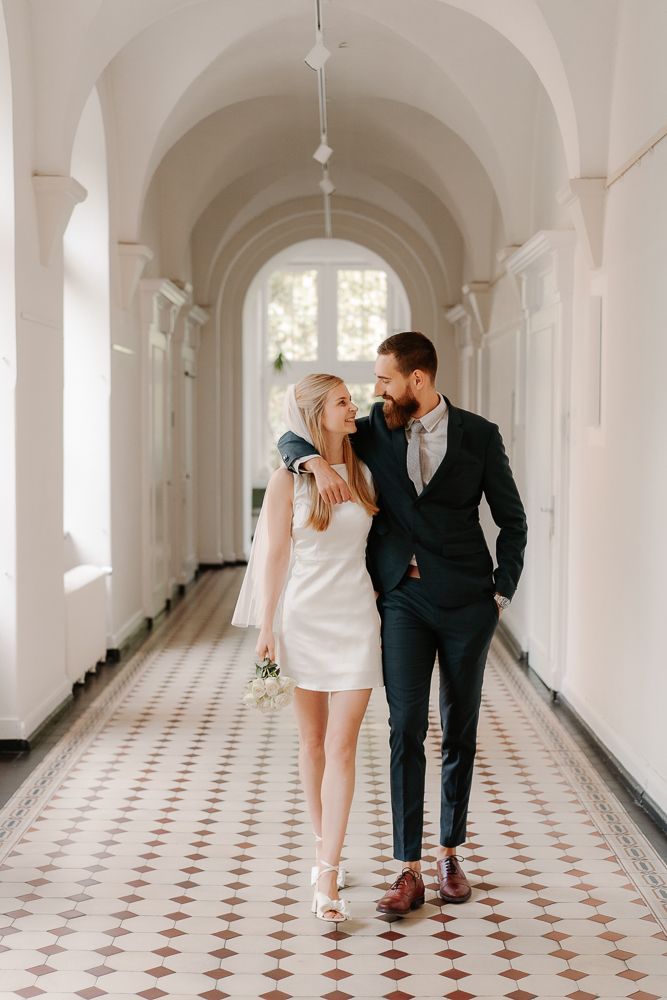 Couple walks and poses together in elegant white arched hallway with patterned tile floors.