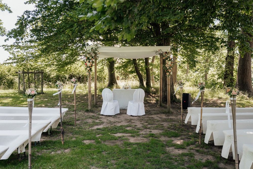 Outdoor wedding ceremony setup with white chairs and a wooden pergola in a garden setting.