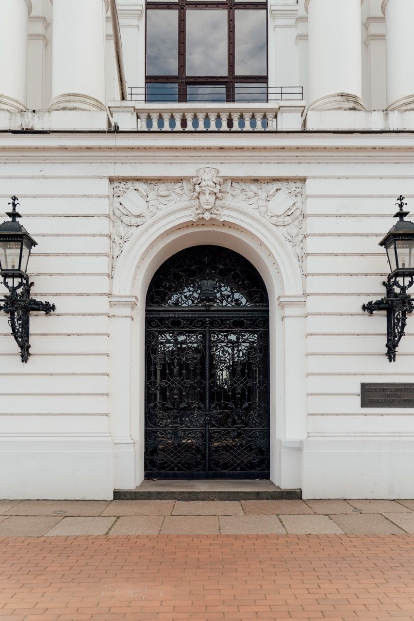 Ornate black wrought iron gates with decorative details set in white stone archways of a classical building facade.