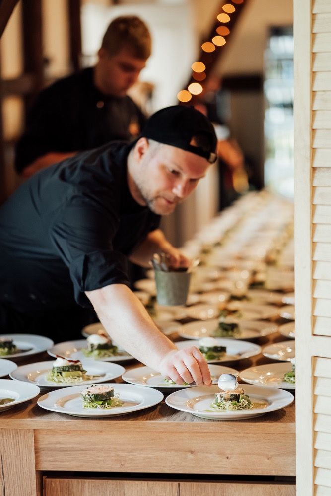 Chef plating elegant dishes on wooden table with warm lighting and restaurant ambiance.