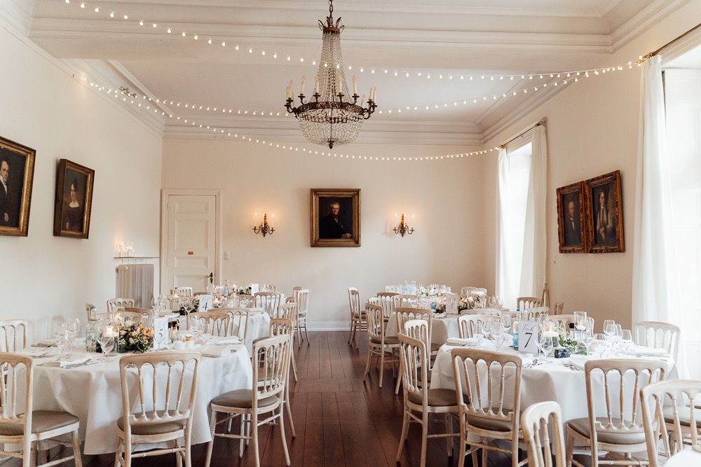 Elegant white banquet hall with round tables, chandeliers, and classic portraits adorning the walls for a wedding reception.