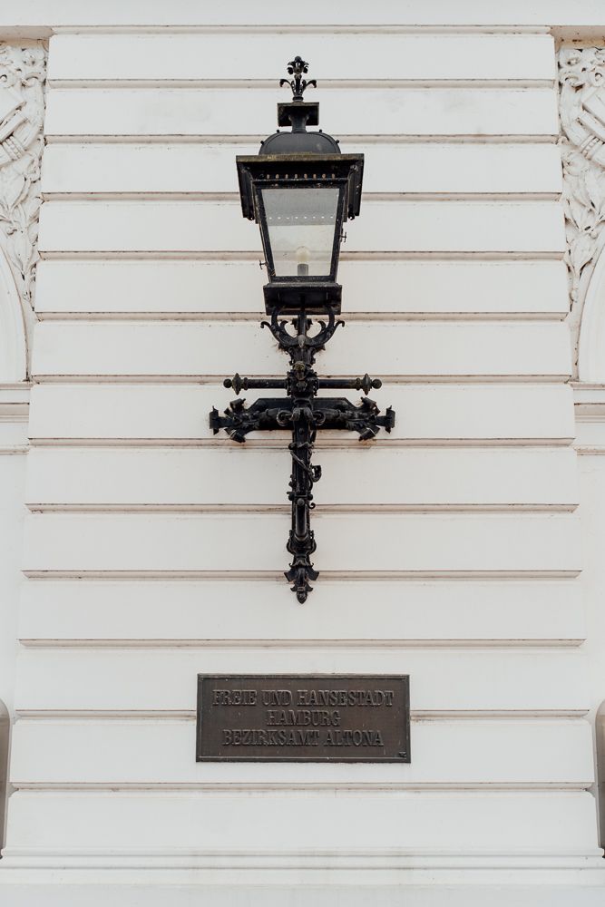 Ornate black iron gas lamp mounted on white wall with decorative architectural details and bronze plaque.