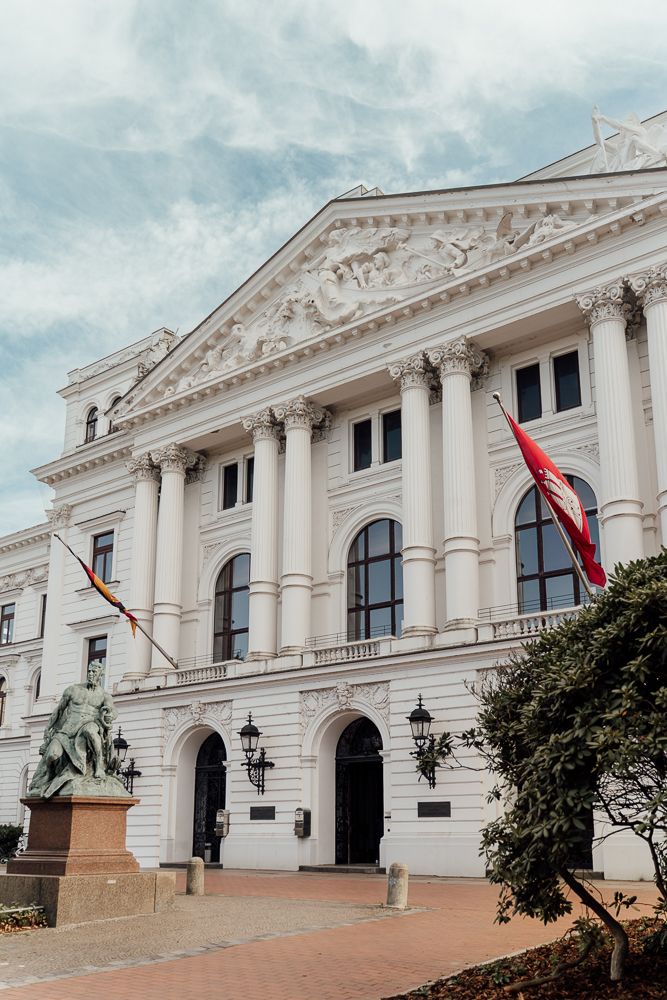 Neoclassical white government building with ornate columns and decorative pediment against cloudy sky.