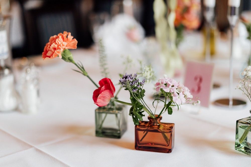 Wedding reception table decorations feature delicate floral arrangements in amber glass vases with soft pink accents.