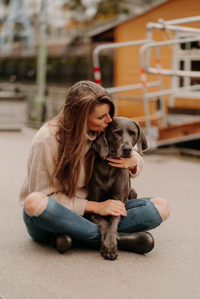 Grauer Hund und Besitzer teilen liebevolle Momente, während sie auf dem Bürgersteig in der Nähe eines orangefarbenen Gebäudes sitzen.