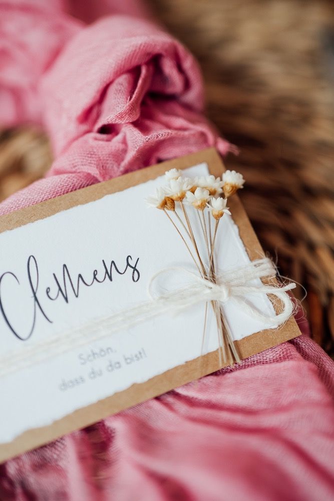Wedding place cards with delicate dried flowers and calligraphy text on white paper with pink fabric accents.