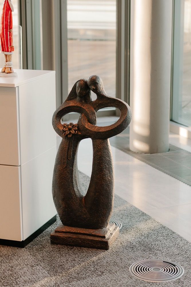 Five identical wooden sculptures of abstract curved shapes displayed in sequence along a window-lit interior space.