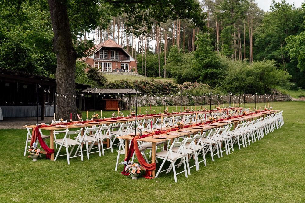 White wooden chairs with red cushions arranged in rows on a grassy lawn for an outdoor wedding ceremony.