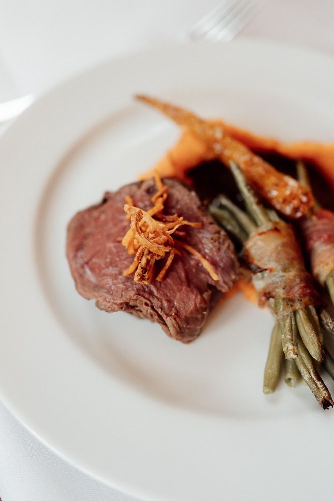 A close-up view of sliced beef tenderloin with green beans and crispy garnish on a white plate.