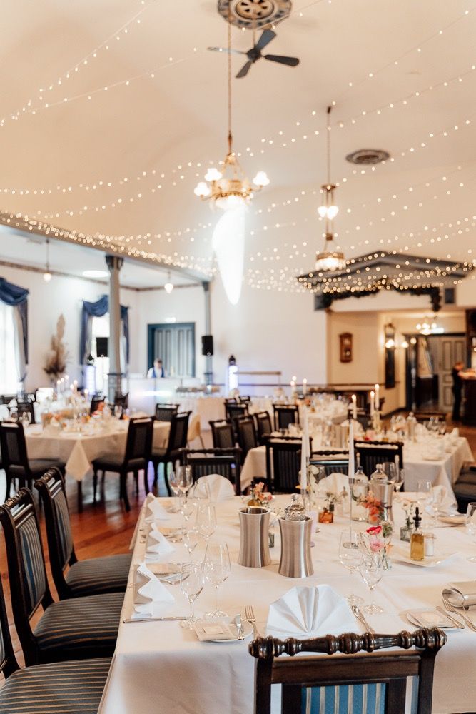 Elegant wedding reception venue with white linens, black chairs, and twinkling string lights decorating the ceiling.