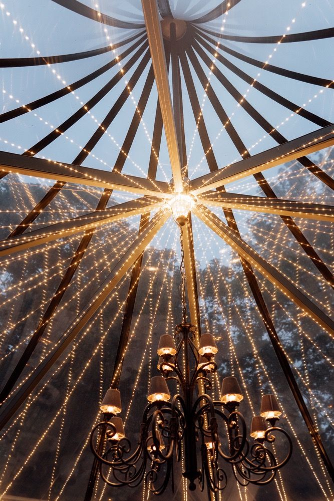 String lights and chandeliers create a magical canopy under a tent ceiling at dusk, forming radiating patterns of light.