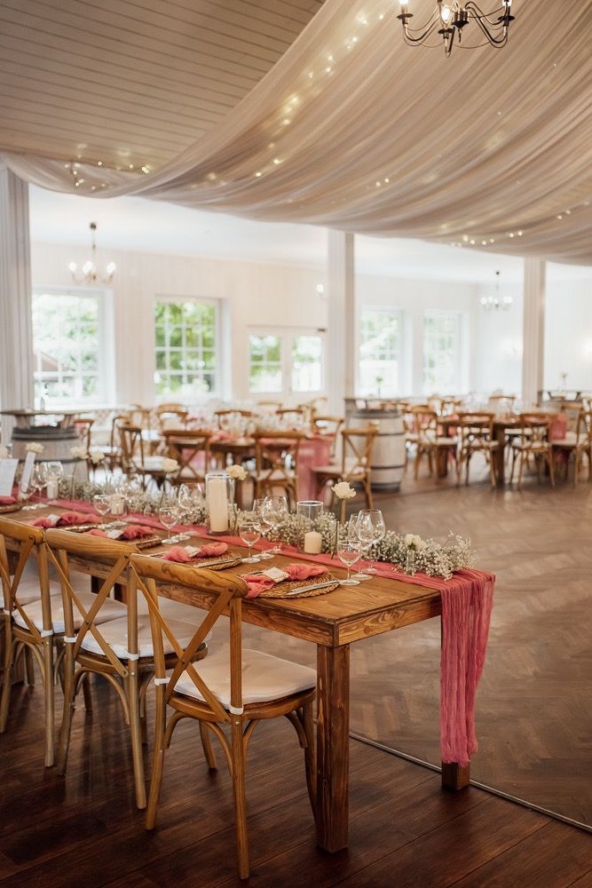 Elegant wedding reception venue with draped white fabric ceiling, rustic wooden tables, and crossback chairs.