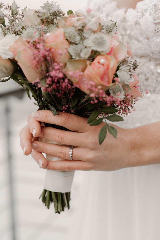Close-up series of hands holding a delicate pink and white wedding bouquet with a diamond engagement ring.