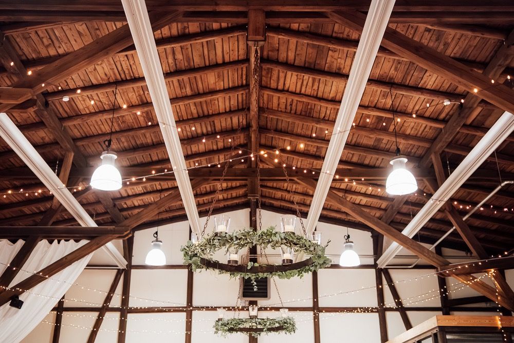 Wooden barn interior ceiling with exposed beams, hanging lights and a decorative floral wreath chandelier.