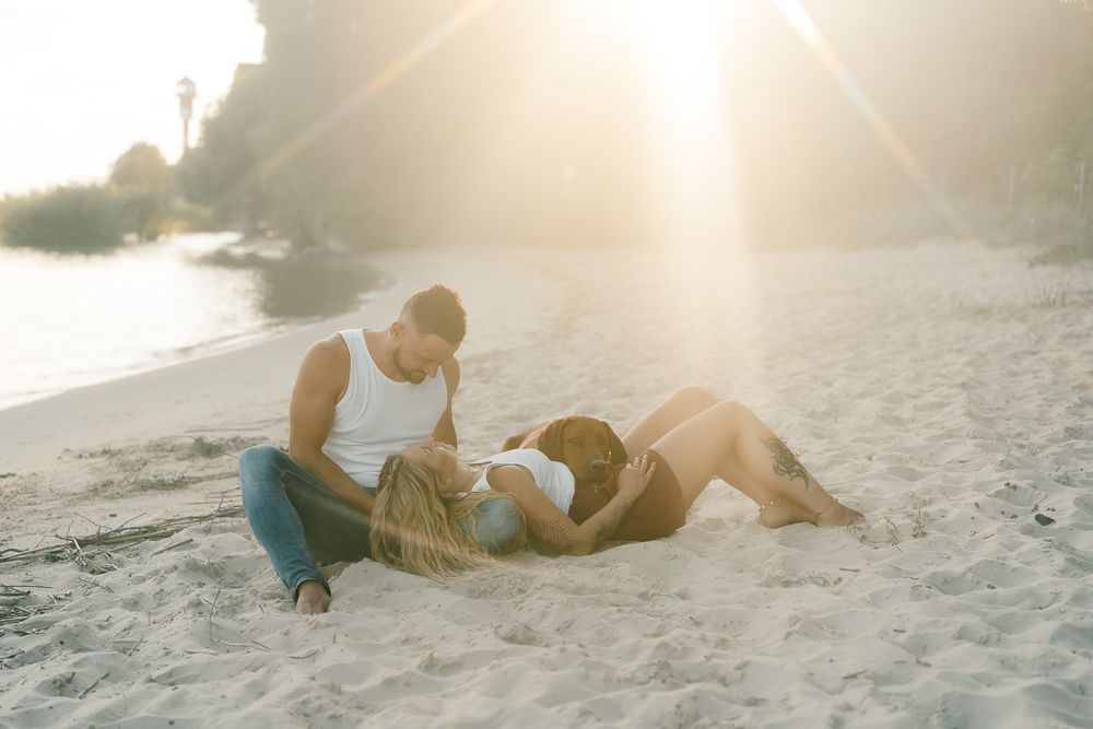 Romantic beach photoshoot with couple and brown dog at sunset.