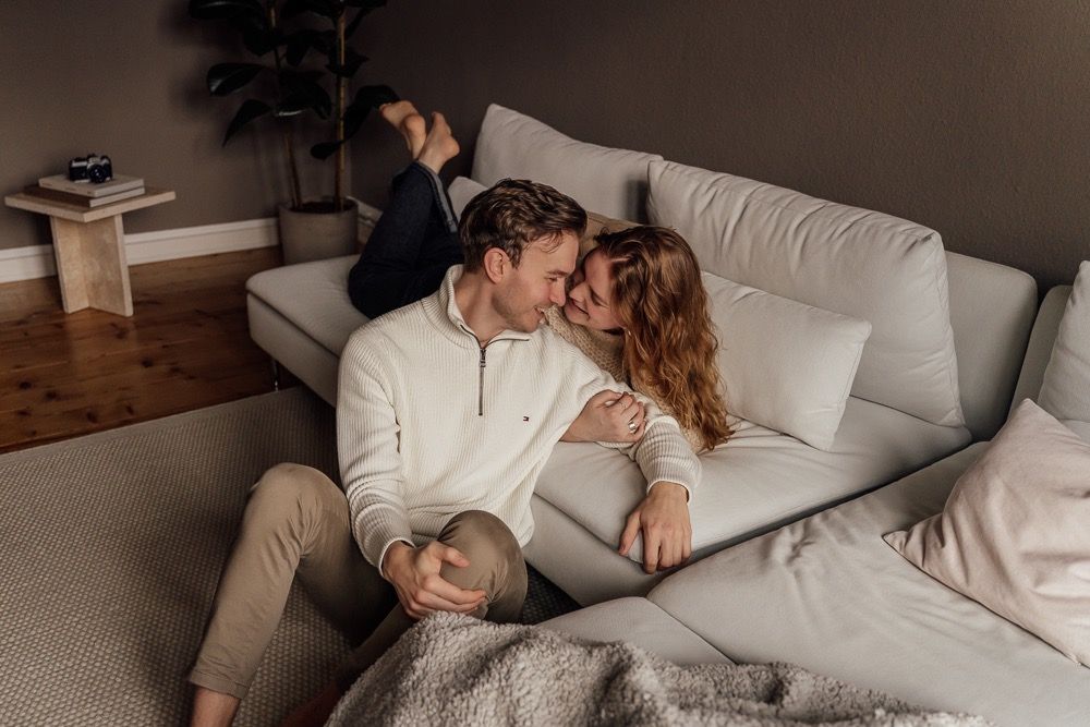 Couple relaxes together on white couch in cozy living room with soft natural lighting.