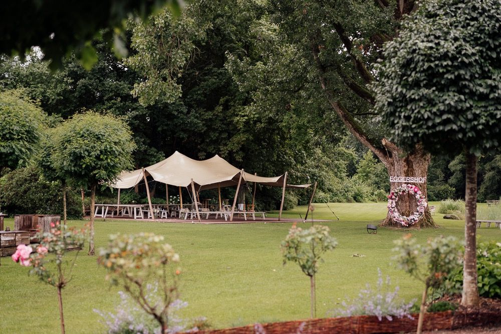 Lush green outdoor garden venue with white tent and trees perfect for a summer wedding celebration.