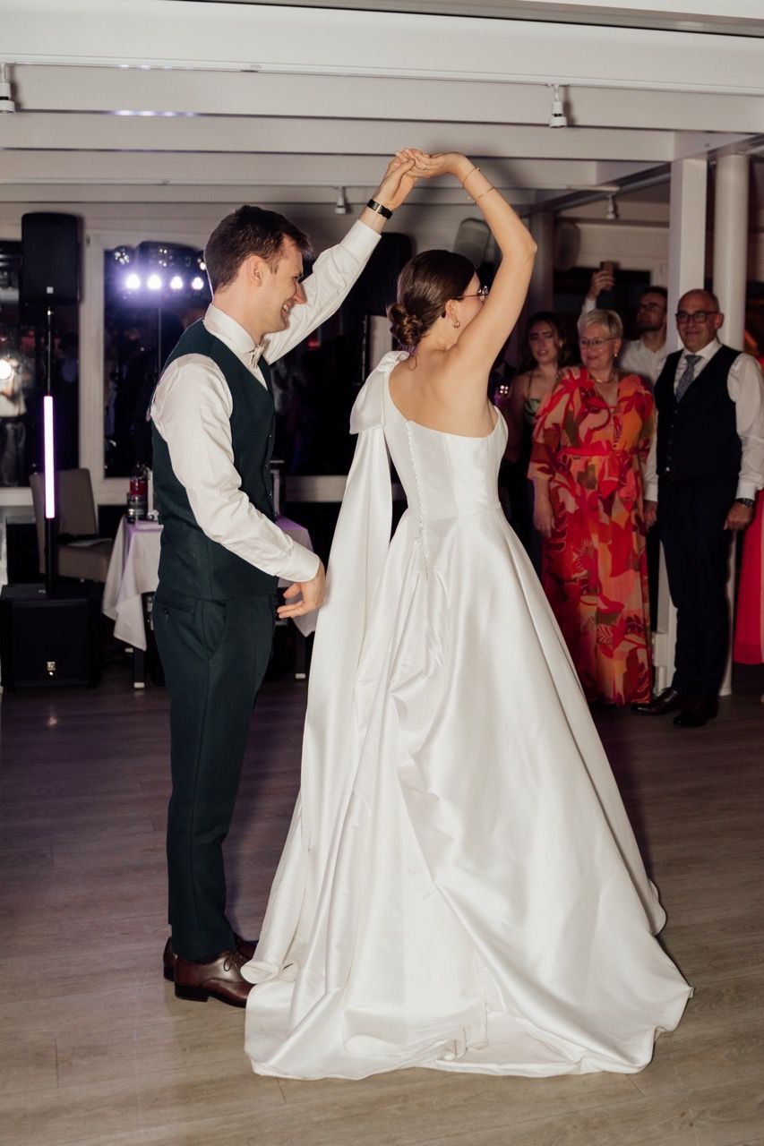 Bride and groom share their first dance, with the bride in a white gown being twirled by the groom in a dark suit.