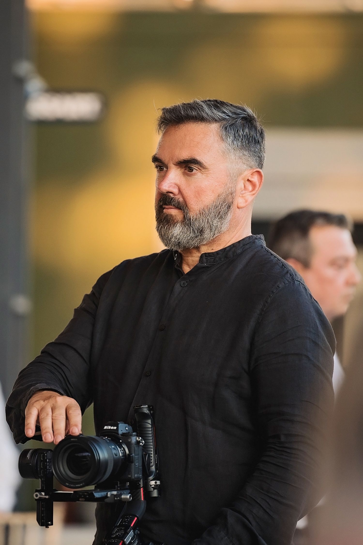 Professional photographer with gray beard holding camera while working at outdoor event.