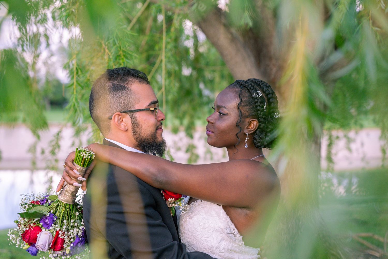 A romantic outdoor wedding scene with a couple embracing under green leaves and natural light.