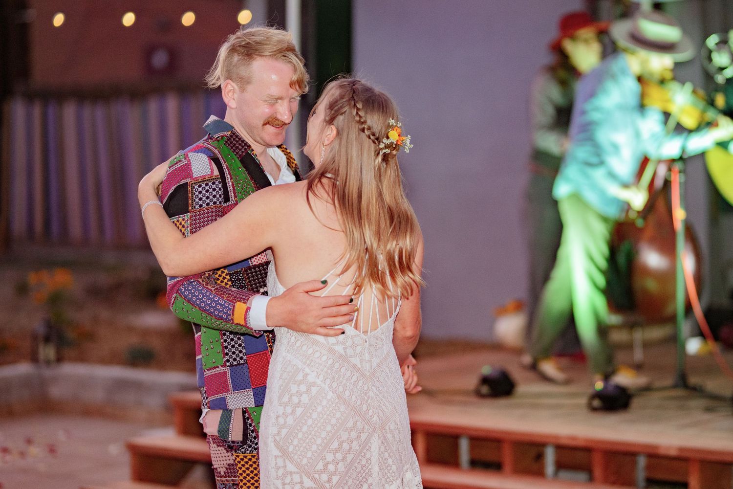 A couple shares a romantic dance together during a wedding reception with colorful lights in the background.