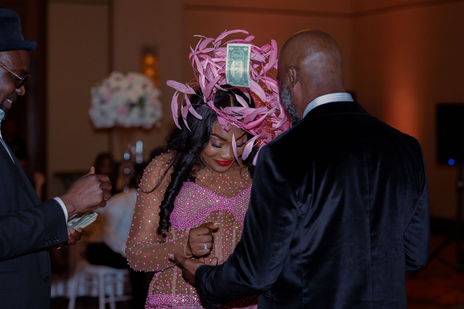 A person in a pink sequined dress and matching headpiece dances at an elegant indoor event.