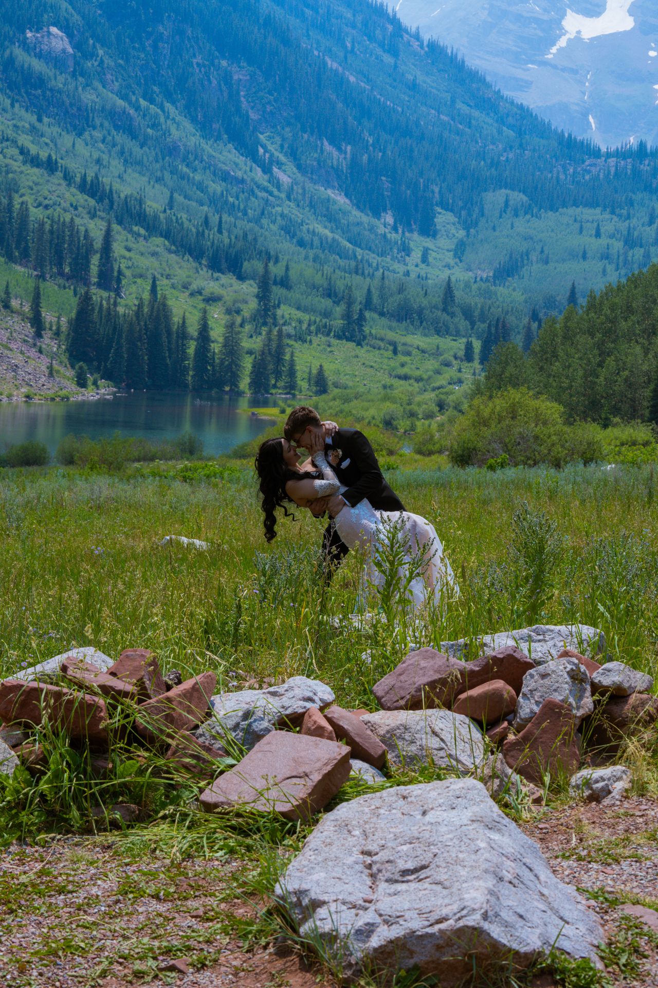 Couple sharing a romantic kiss in a green mountain valley by a lake and pine forest.