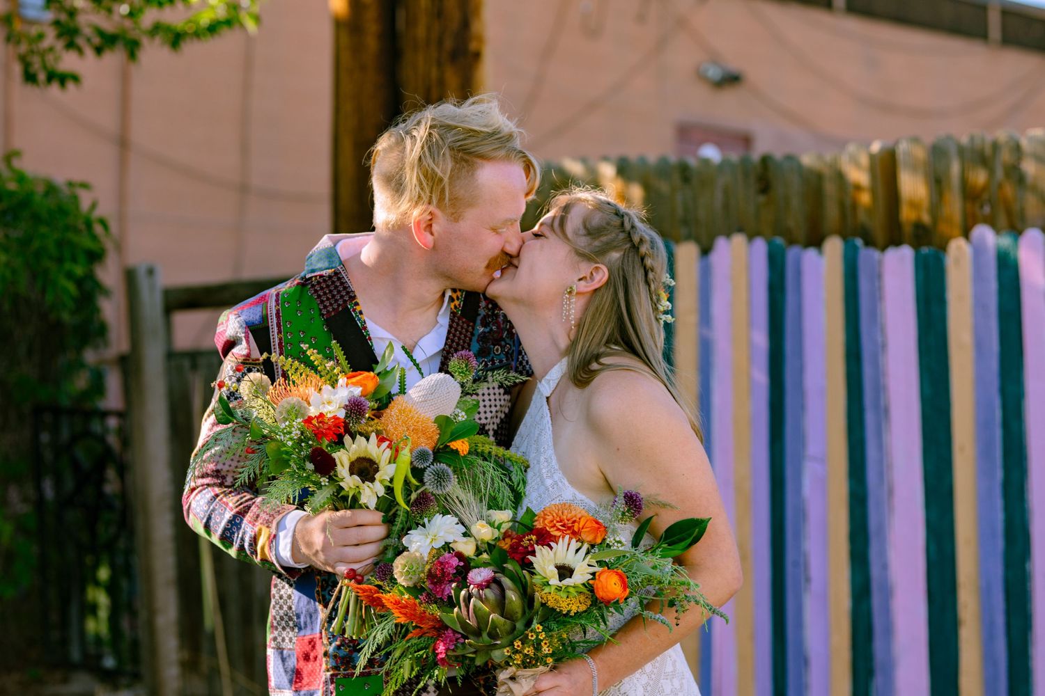 Wedding couple shares intimate moments in garden setting with vibrant orange and green floral arrangements.